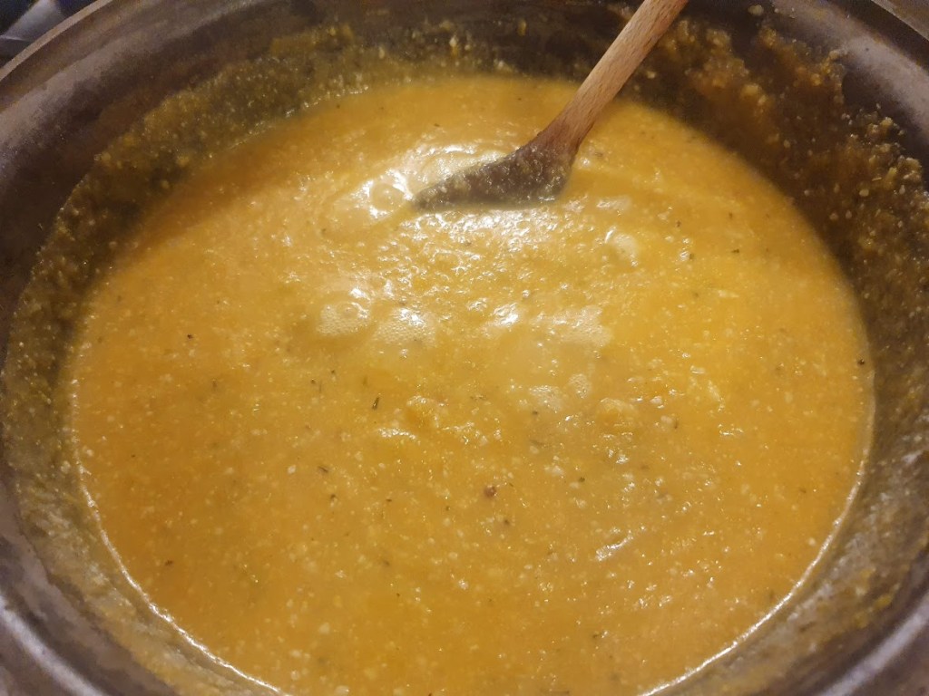 Butternut squash soup in the pot with a wooden spoon.