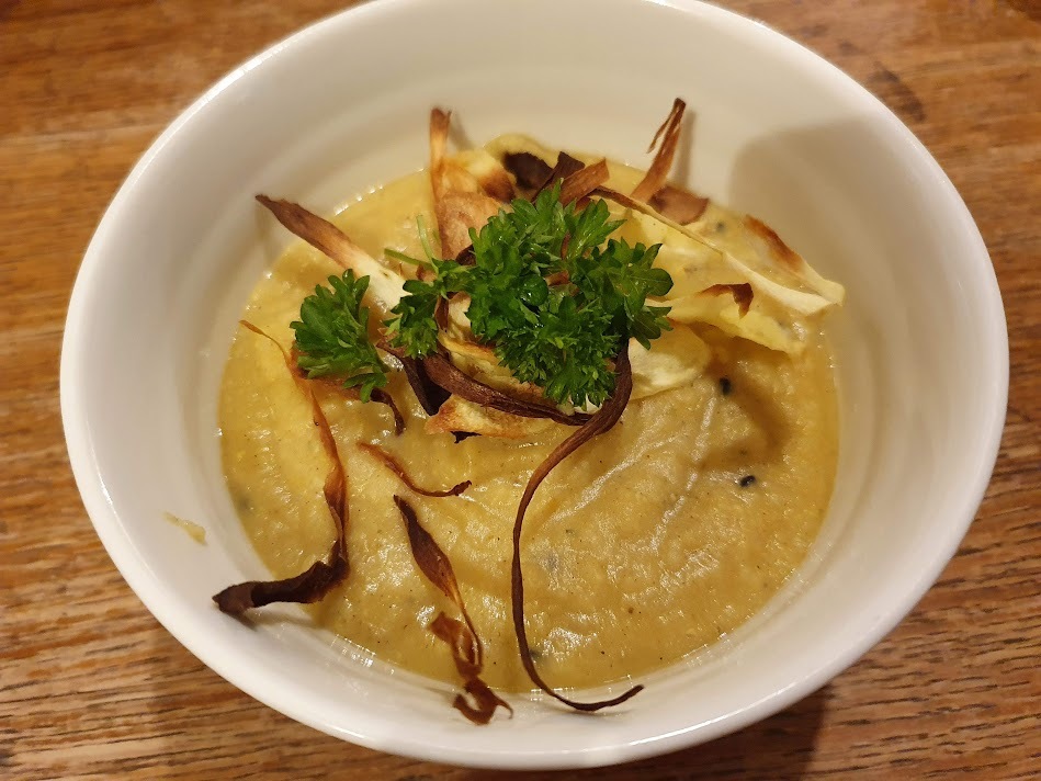 Red lentil and parsnip soup with parsnip chips and parsley on the top.