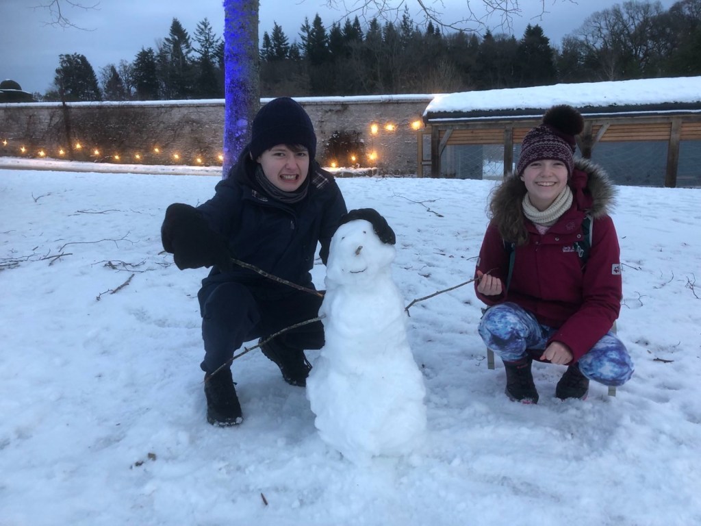 The kids kneeling next to their snowman.