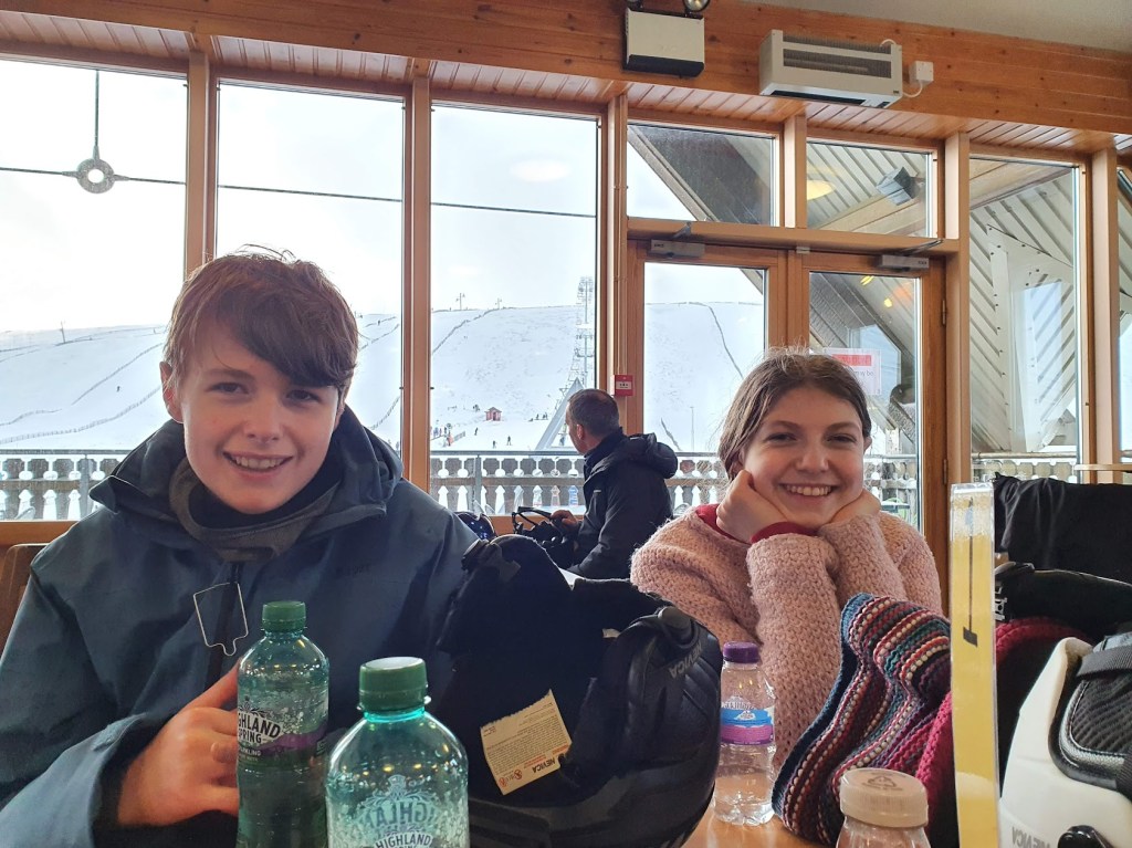Daniel and Elizabeth in the cafe with ski slopes behind them.