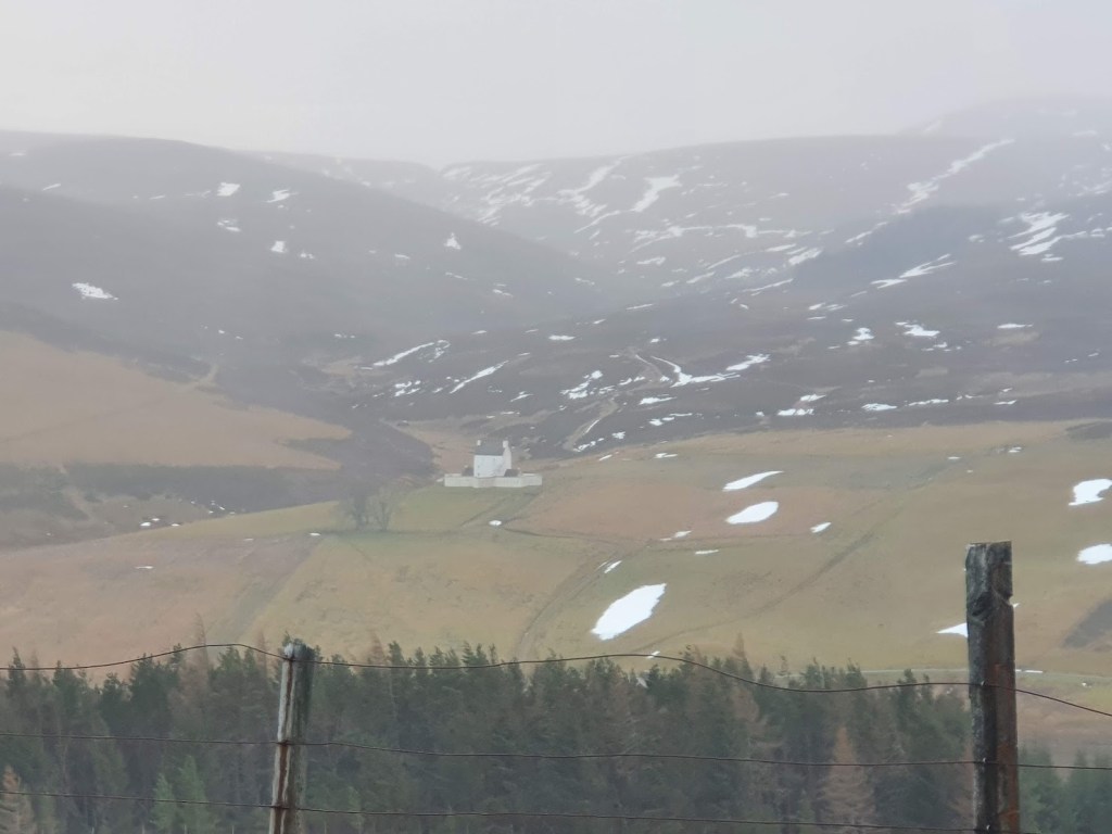 Corgarff Castle from a distance with patches of snow on the surrounding landscape.