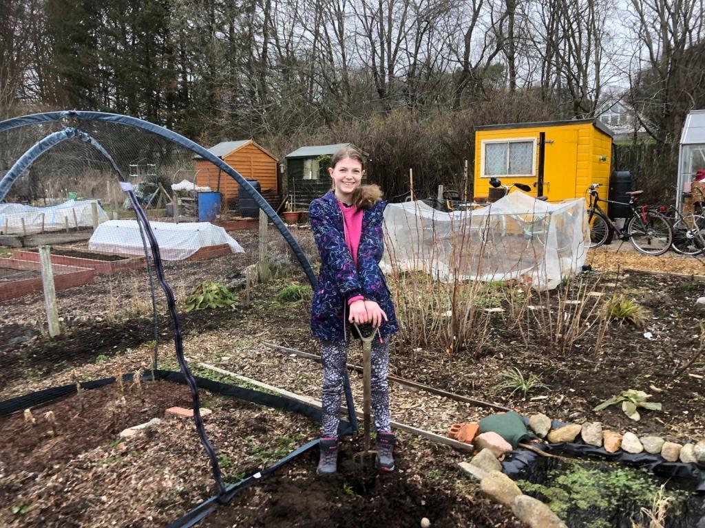 Elizabeth proudly standing with a shovel over a freshly dug garden bed.