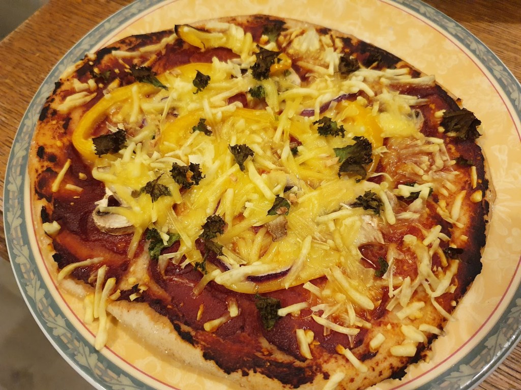 Elizabeth's pizza topped with yellow pepper, vegan cheese, mushrooms, kale, and cherry tomatoes