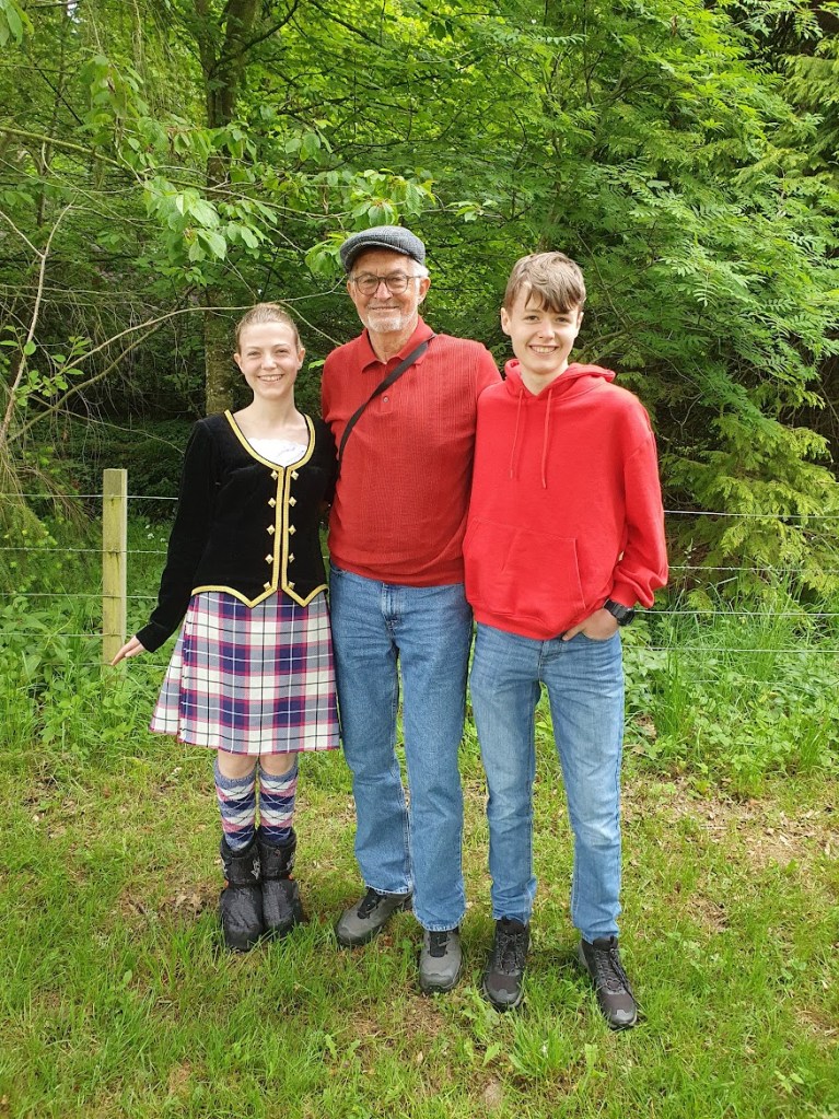 Elizabeth, Grandad, and Daniel smiling in front of a forest.
