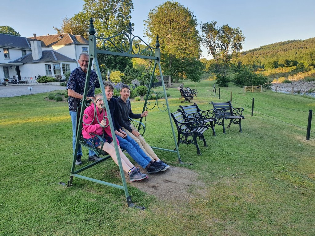Grandad pushing Elizabeth, Daniel, and Etienne on a swing outside the restaurant.