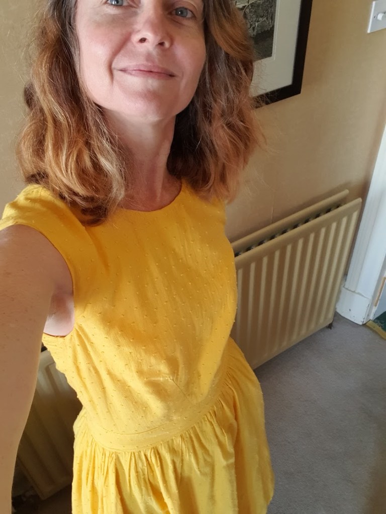 Rachel wearing a yellow dress that has a full circle skirt, is fitted at the top and has button detailing on the back - selfie from above