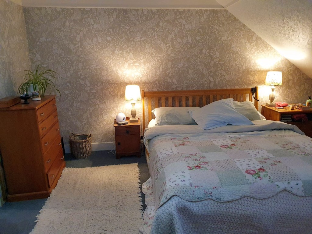 The bedroom with a sage green wallpaper behind the bet that has foliage and British animals - foxes, squirrels, birds.