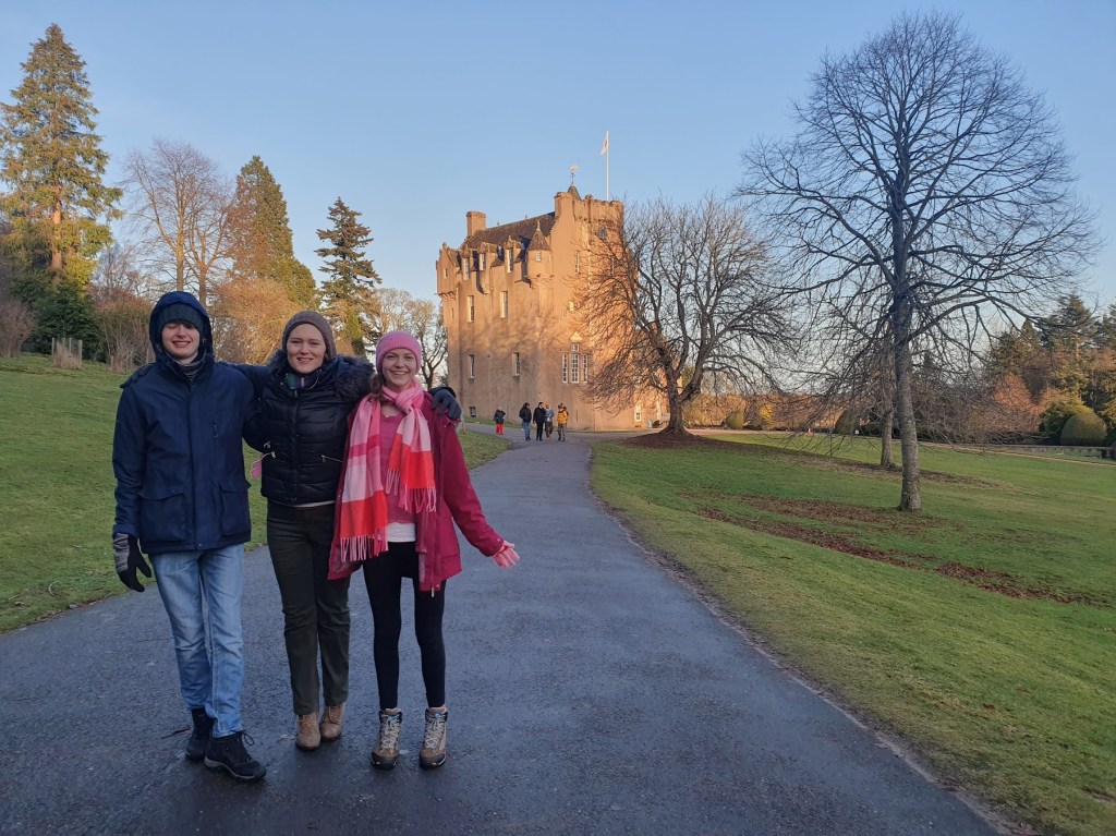 Cara, Daniel, and Elizabeth stading in from of Crathes Castle. The sky is blue and cloudless.