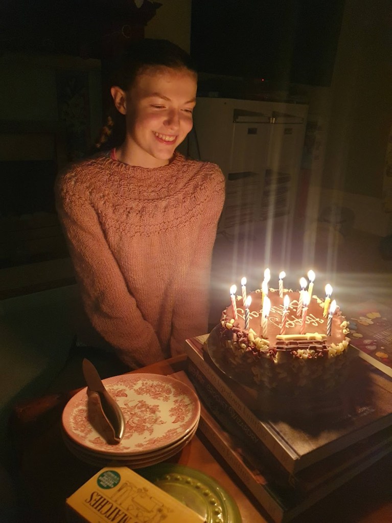 Elizabeth looking at her birthday cake. It's chocolate with 14 candles.