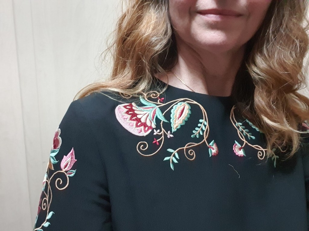 Close-up of the embroidery near the neckline. It's pink and green flowers and vines.