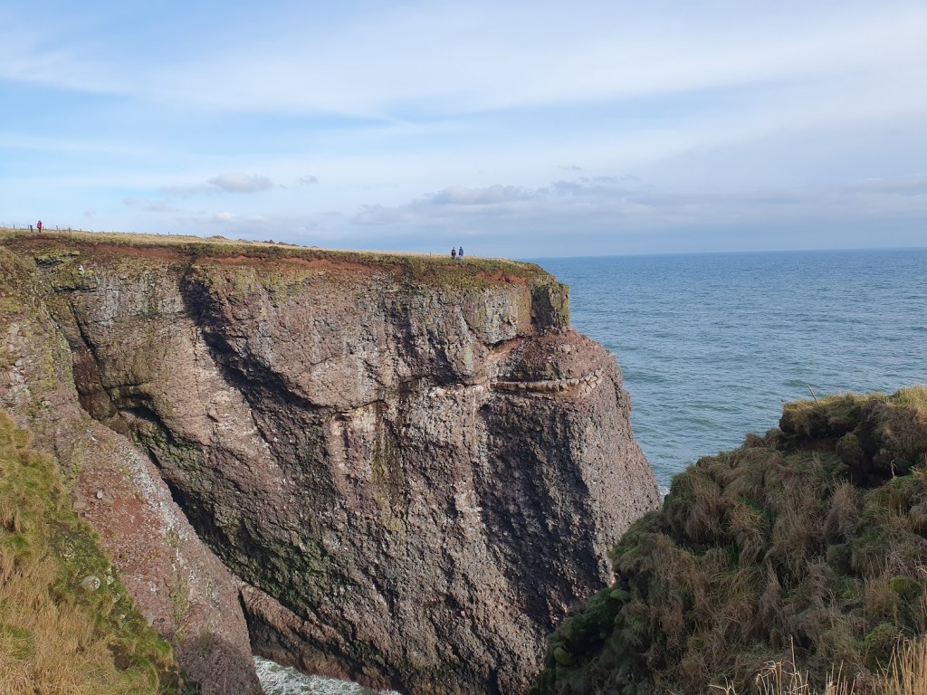 Three small figures on the opposite cliff give a perspective on how high they are. 