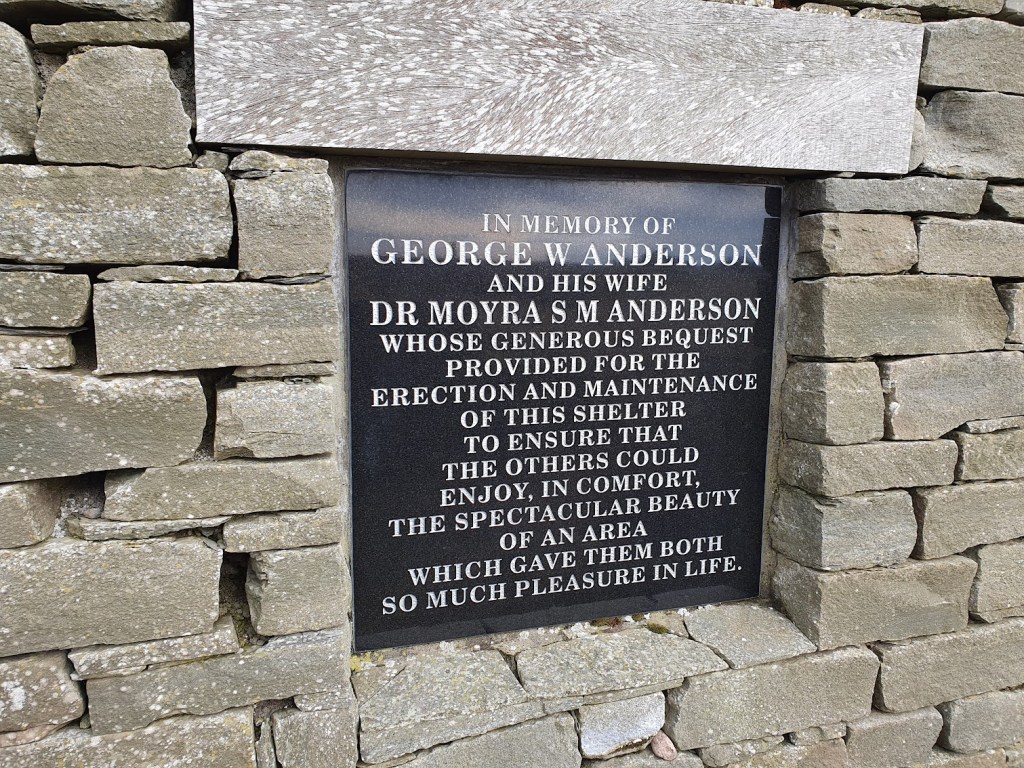 A plaque showing that reads, "In memory of George W Anderson and his wife Dr Moyra S M Anderson whose generous bequest provided for the erection and maintenance of this shelter to ensure that the others could enjoy, in comfort, the spectacular beauty of an area which gave them both so much pleasure in life. "