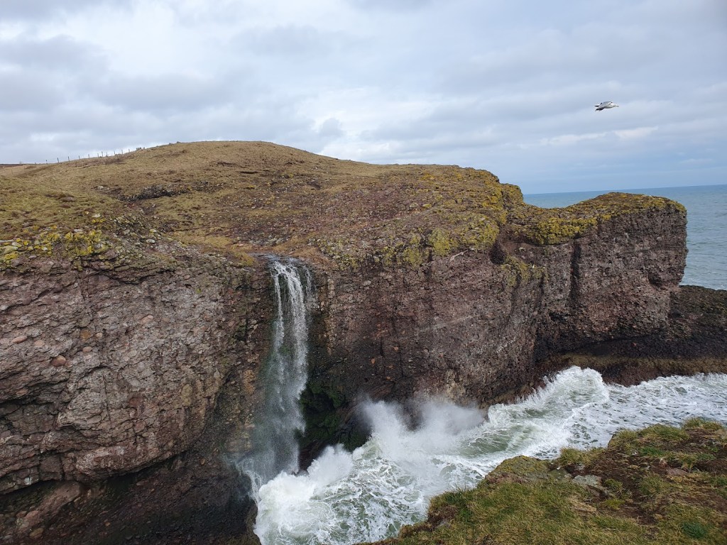 The waterfall at the start of the walk cascading down the cliffs into the choppy sea below. 
