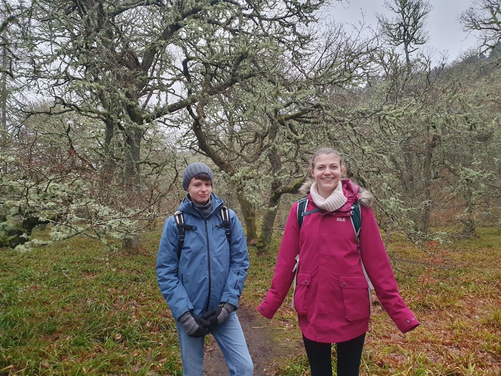 Daniel and Elizabeth in the woods with trees behind them draped in lichen.