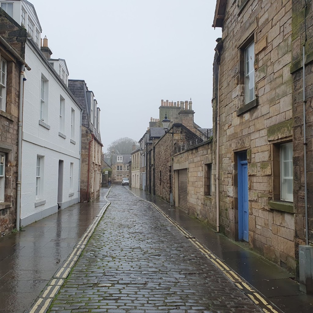 Street in central St Andrews with residential stone buildings on either side of a cobblestone street.