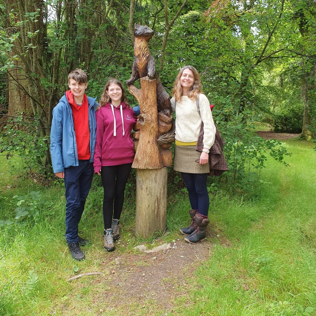 Daniel, Elizabeth, and Rachel standing next to the statue of a pine marten on the grounds at Crathes Castle.