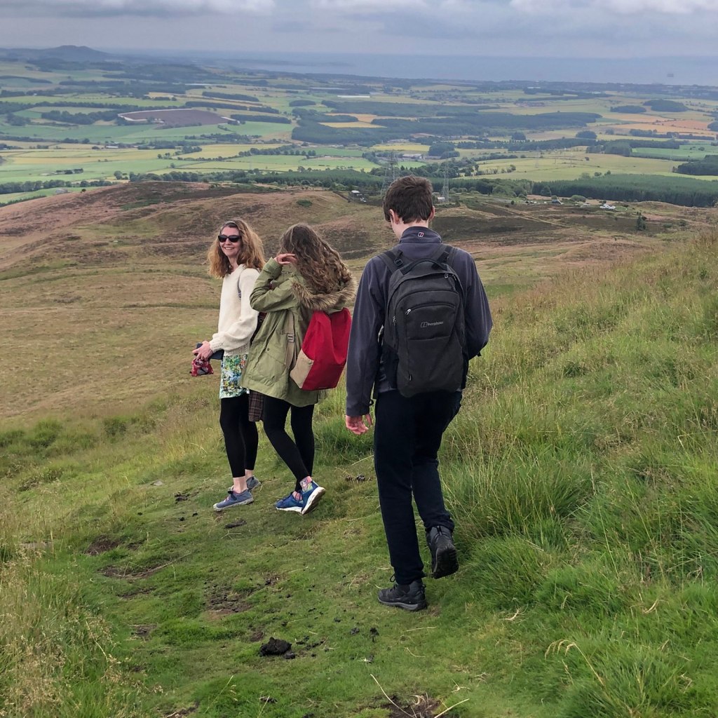 Rachel, Elizabeth and Daniel walking down the hill. Rachel is looking back and smiling.