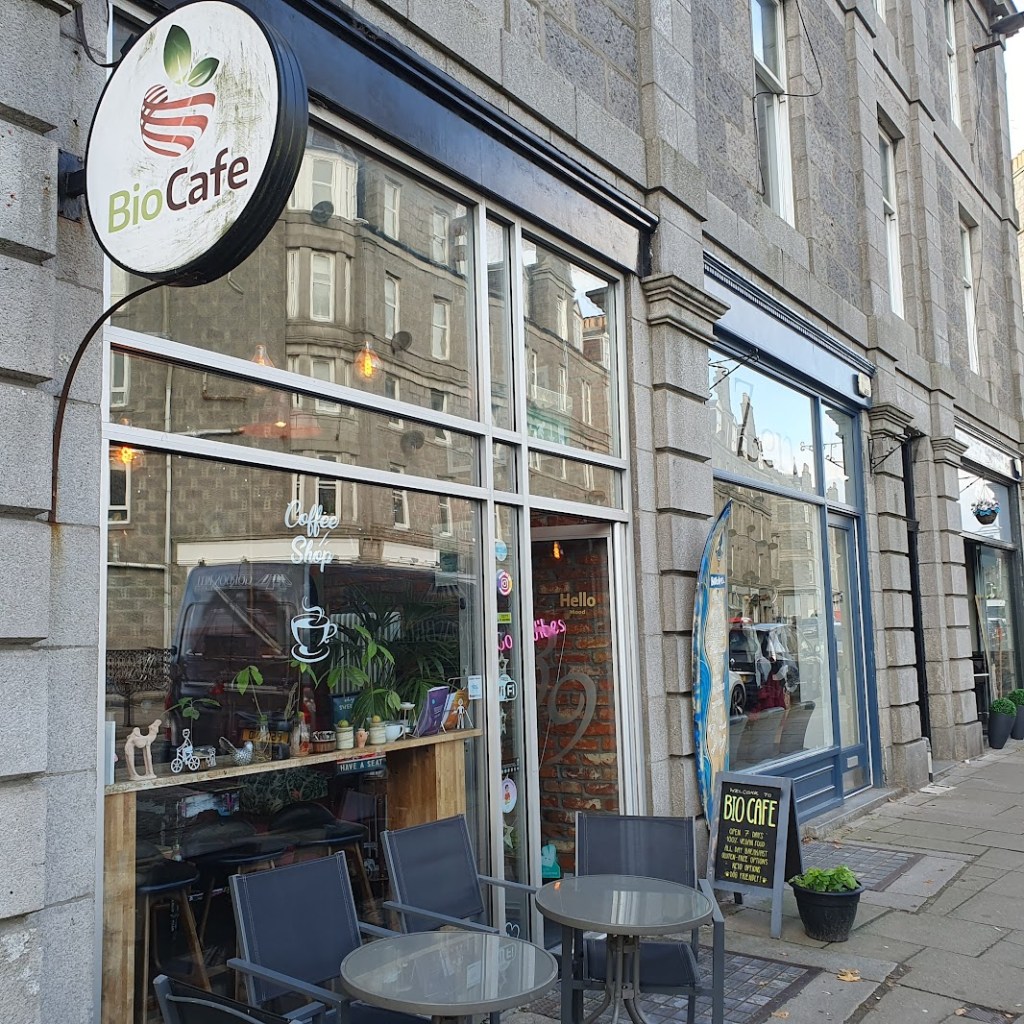 The street front of BioCafe showing a granite building with table seating outside.