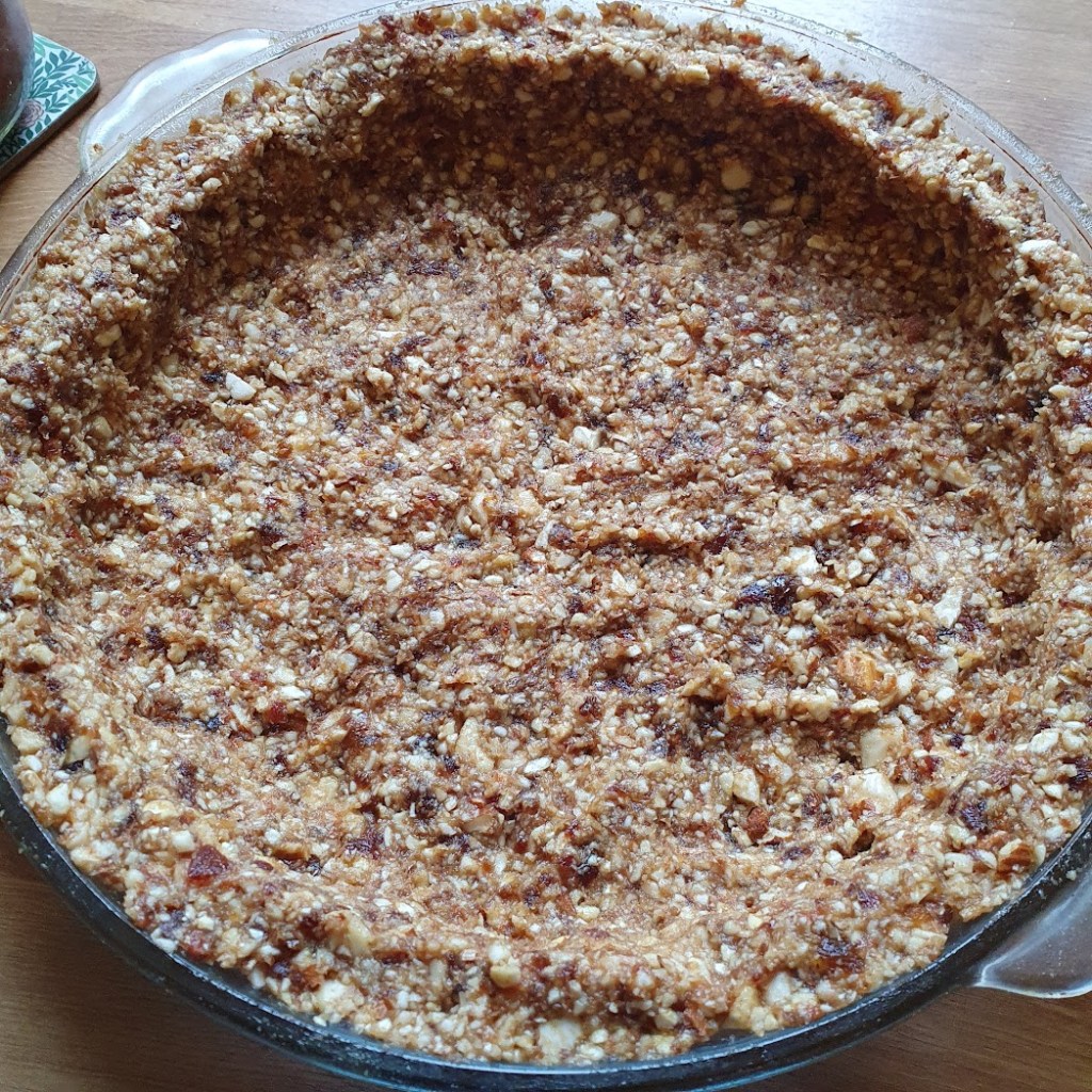 The nutty base for the cheesecake, pressed into a glass dish.