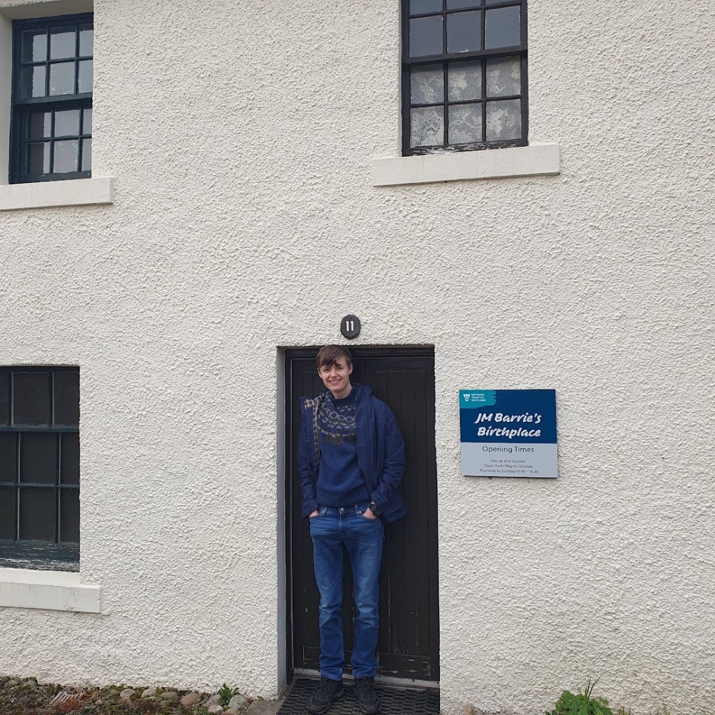 Daniel standing in front of the front door which is too short for him.