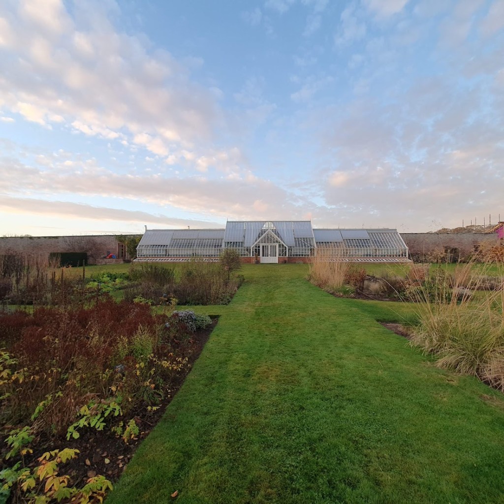 A Victorian glasshouse with planted garden beds in the foreground.