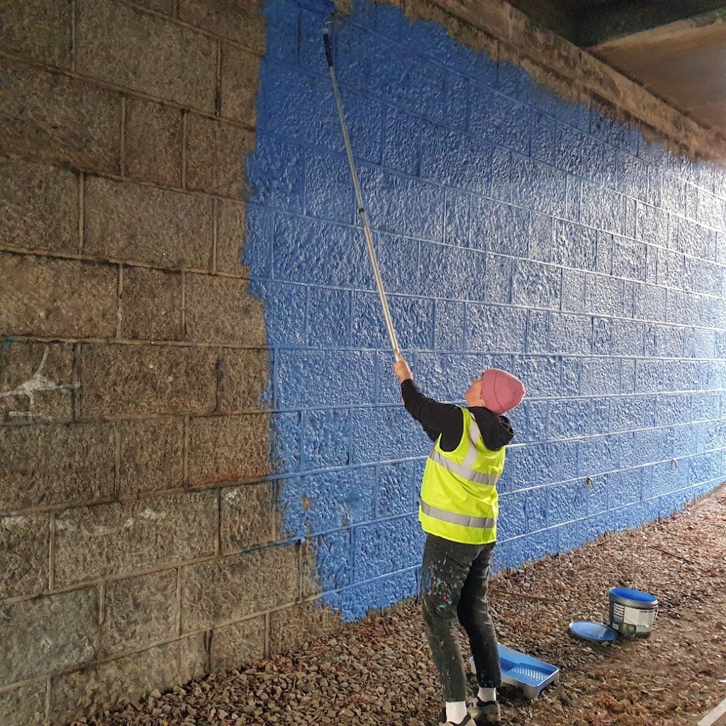 The artist painting the wall blue.