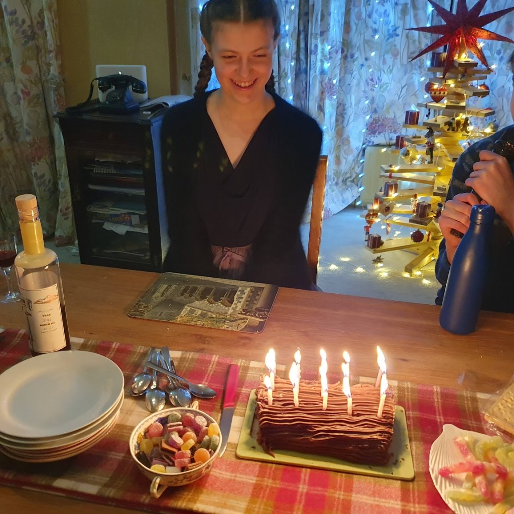 Elizabeth smiling before her chocolate yule log with 15 candles burning.