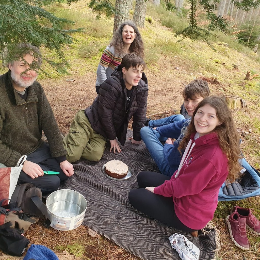 Our party smiling and sitting on picnic rug about to cut the cake.