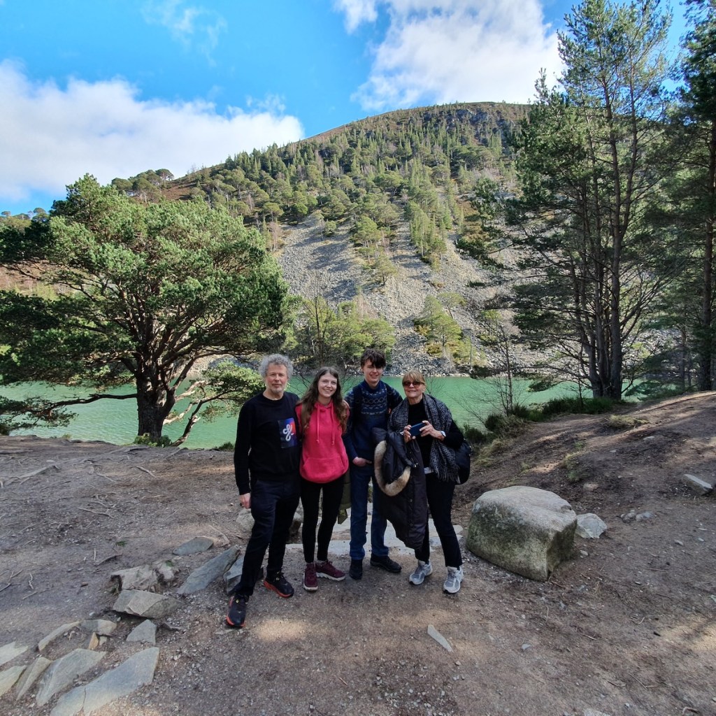 A wide angle shot of Ben, Elizabeth, Daniel and Mum smiling in front the loch.