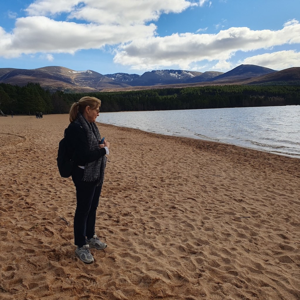 Mum standing on the sand looking at Loch Morlich.