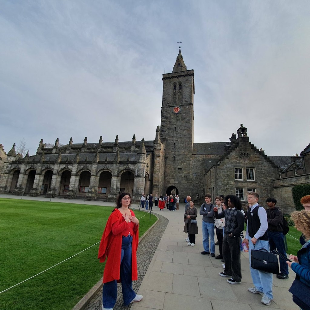Student ambassador in red robe giving a tour beside St Salvator's Chapel, St Andrews.