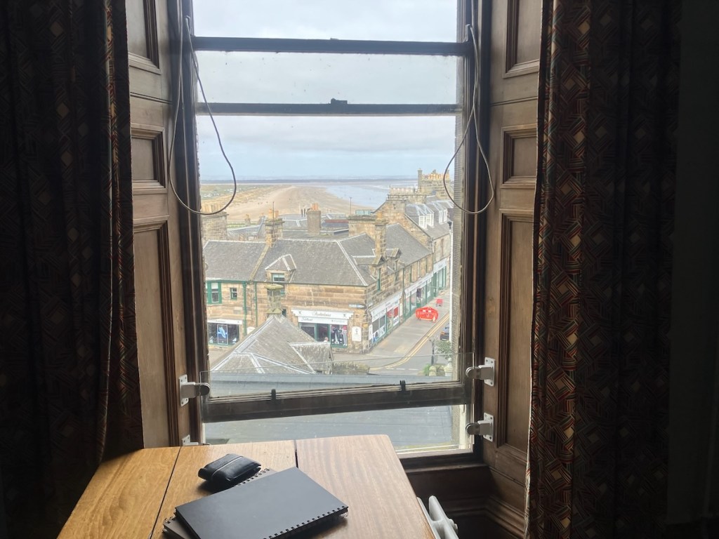 A view from the window which shows a long beach and the sea.