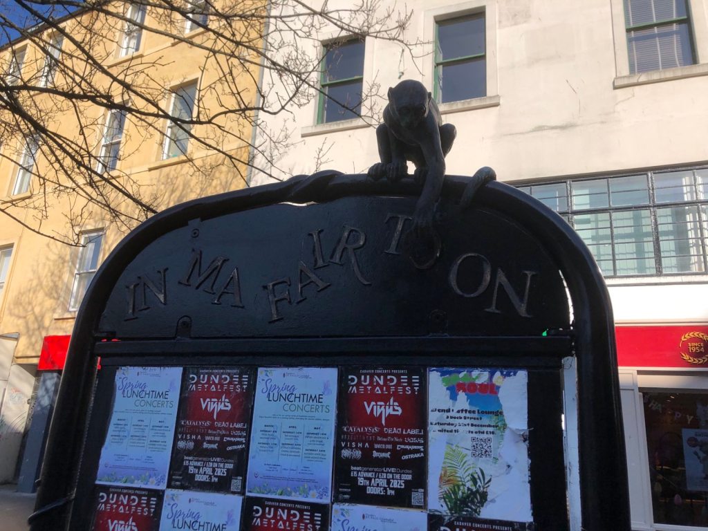 A sign with a monkey sculpture that reads, "In ma fair toon".