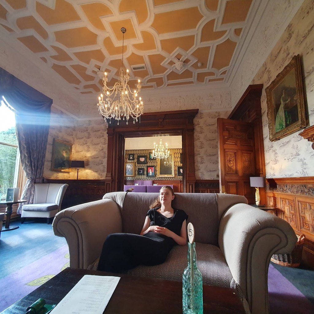A wide angle view of the lounge with the bar in the background and Elizabeth on a sofa in the foreground.