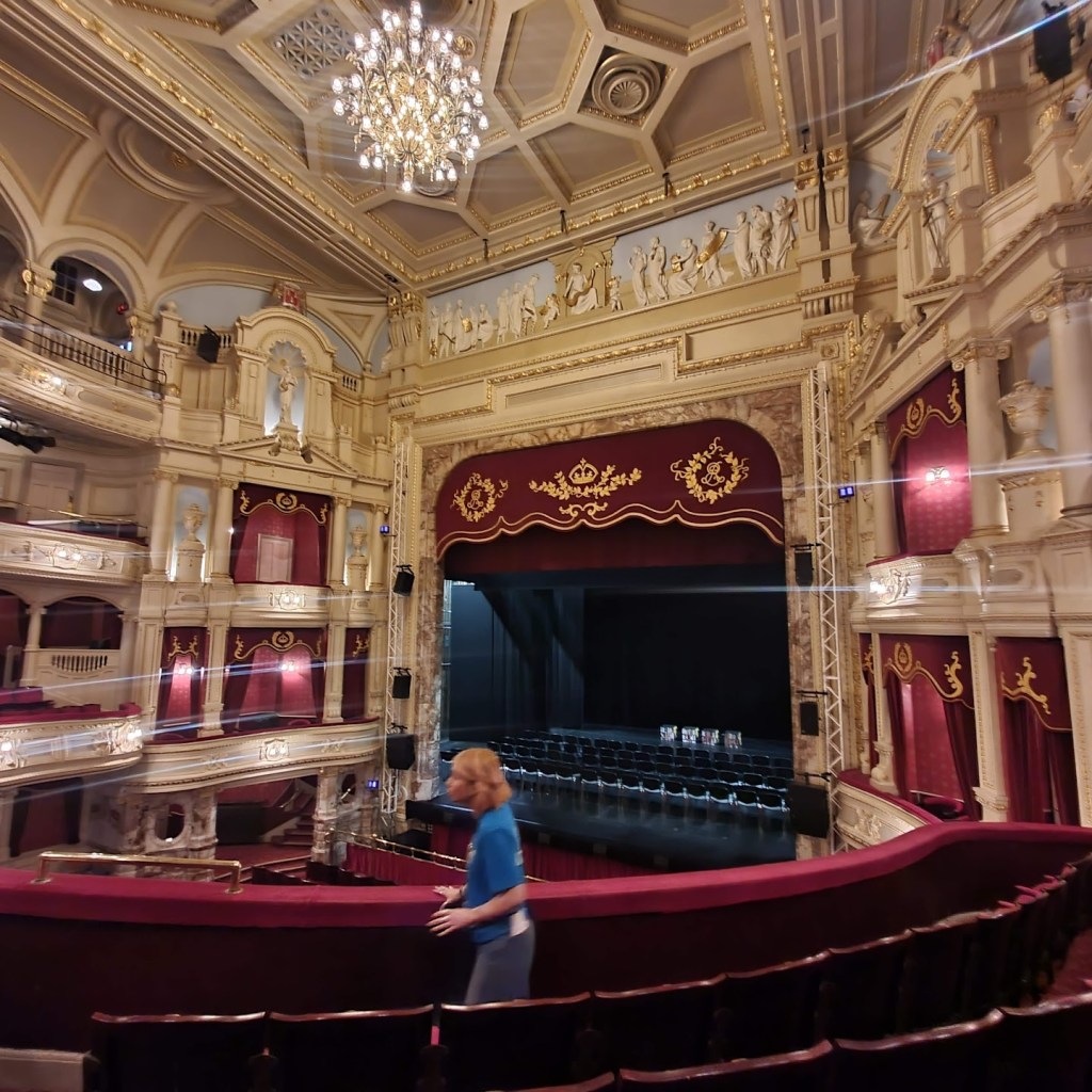 Sitting in the dress circle looking down at the stage. The massive chandelier is visible at the top of the photo.