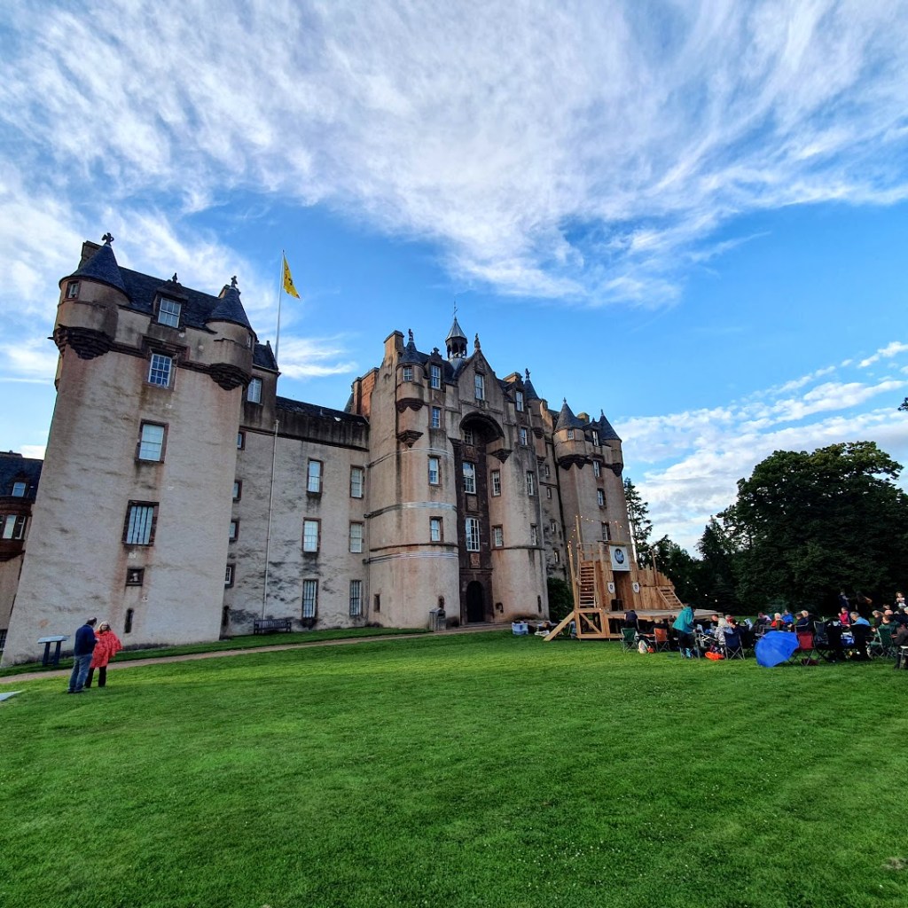 Fyvie Castle with the stage in front, people sitting waiting and a blue sky with scattered clouds.
