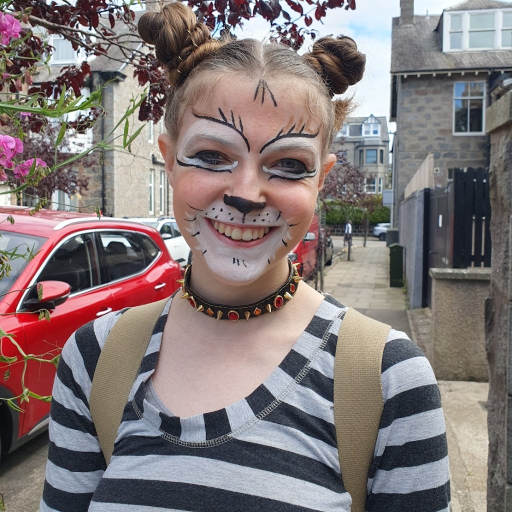A close-up of Elizabeth's makeup which has a white patch around the mouth with whiskers and dark eyebrows.