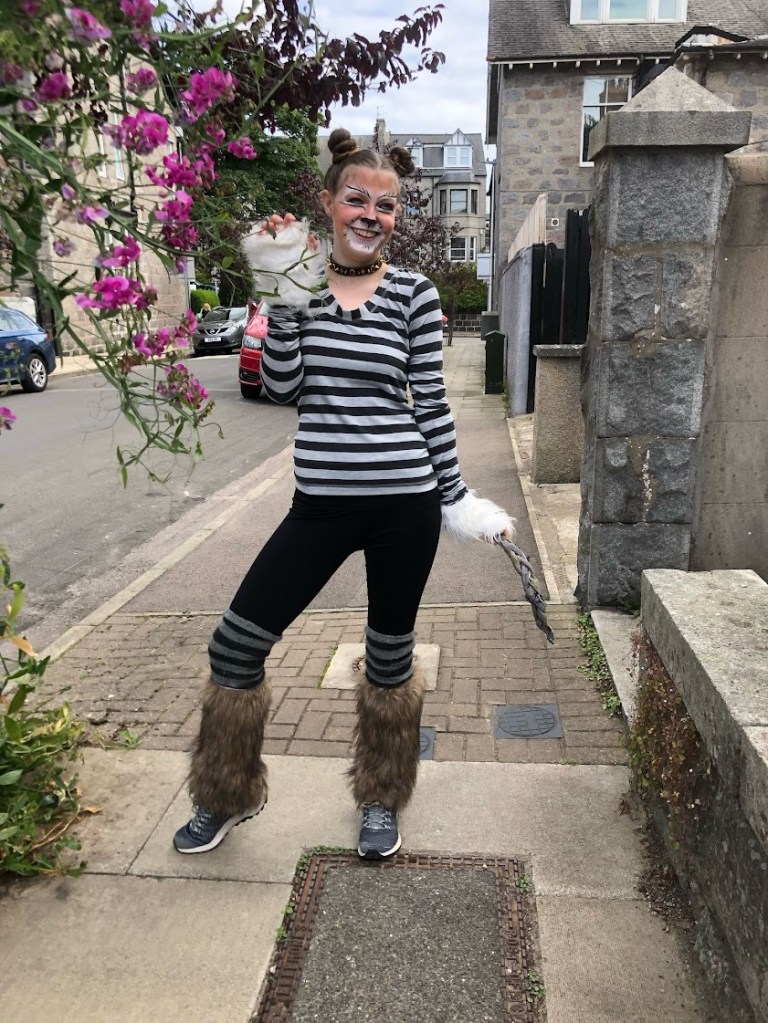 Elizabeth holding her tail and smiling with claws up.