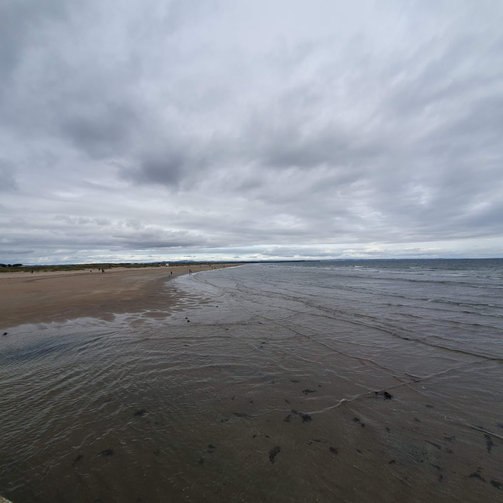 A wide angle of the beach with sand and very little in the way of waves.