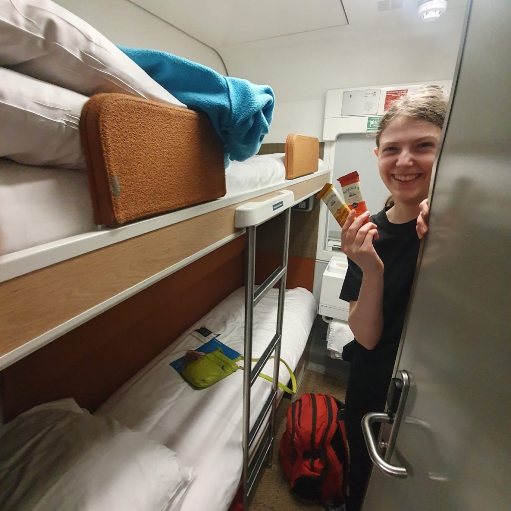 Elizabeth holding two free chocolates in our cabin where you can see two bunk beds and a sink.
