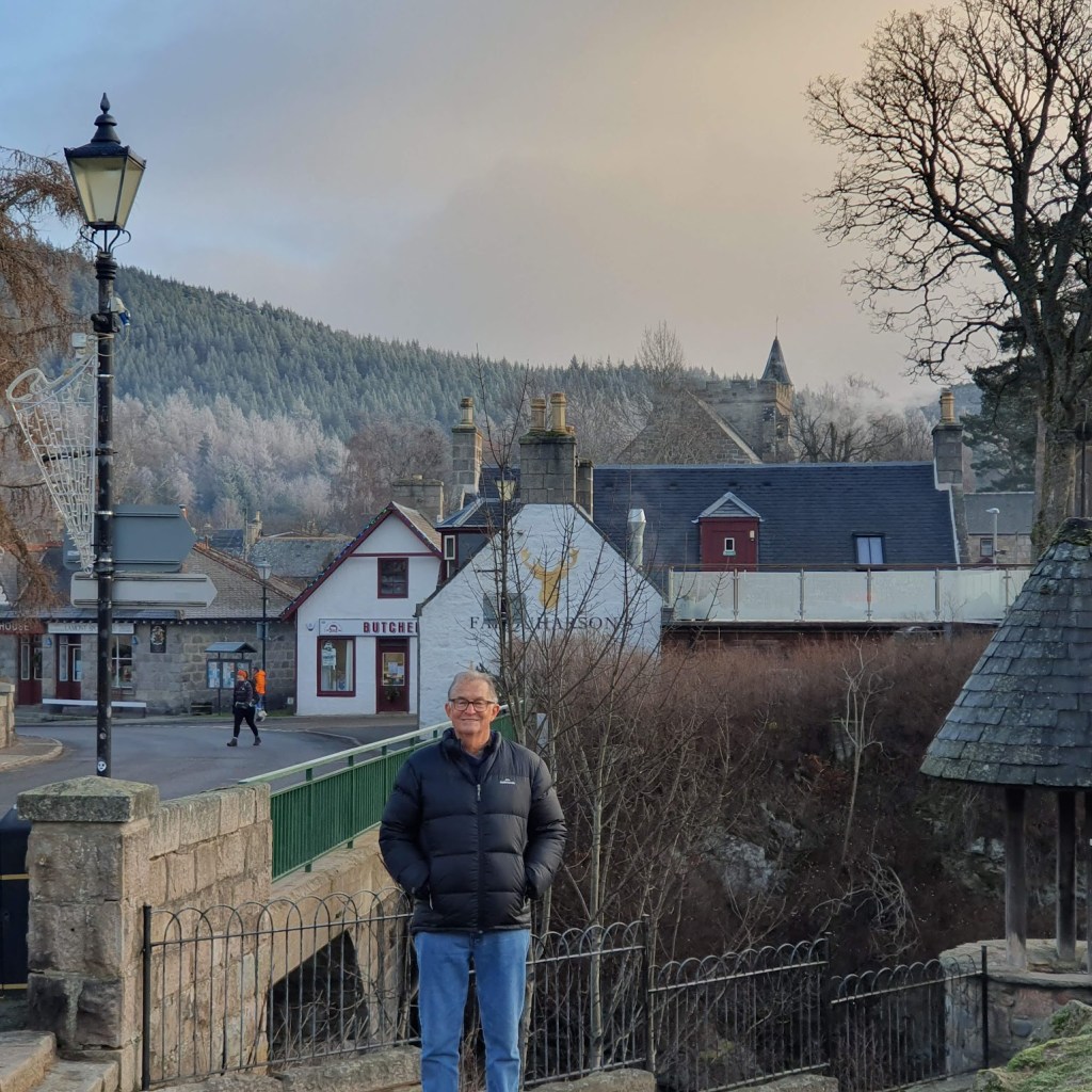 A cold Braemar with Dad in the foreground and silver trees on the hill in the background.