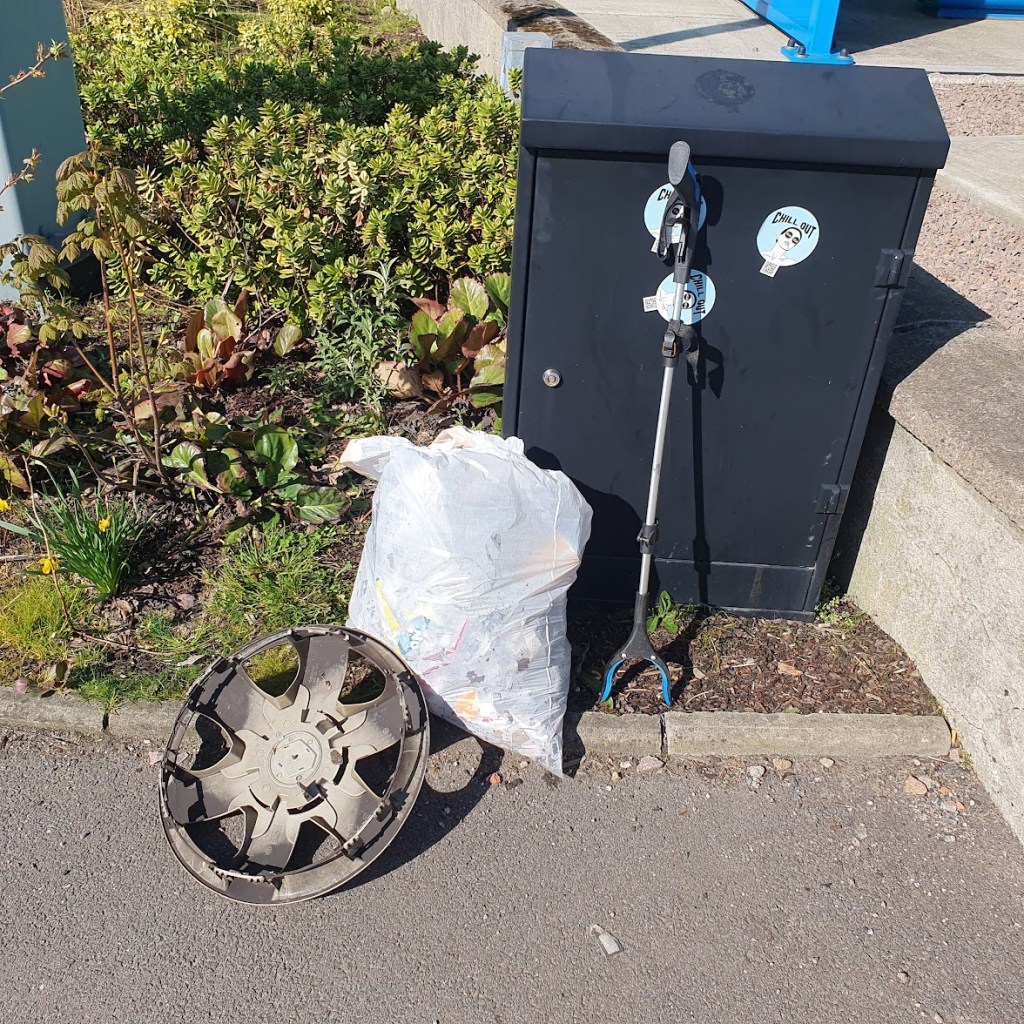 A white bag of rubbish next to the garden plus a hub cap.