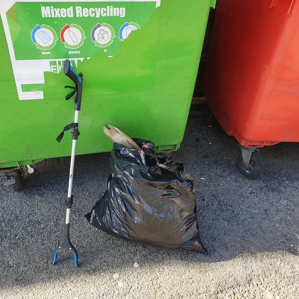 A black bag of litter next to a couple of rubbish bings.