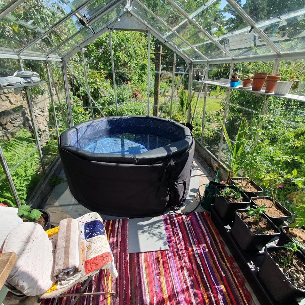 My hot tub in a very sunny greenhouse with some plants in pots on the sides.