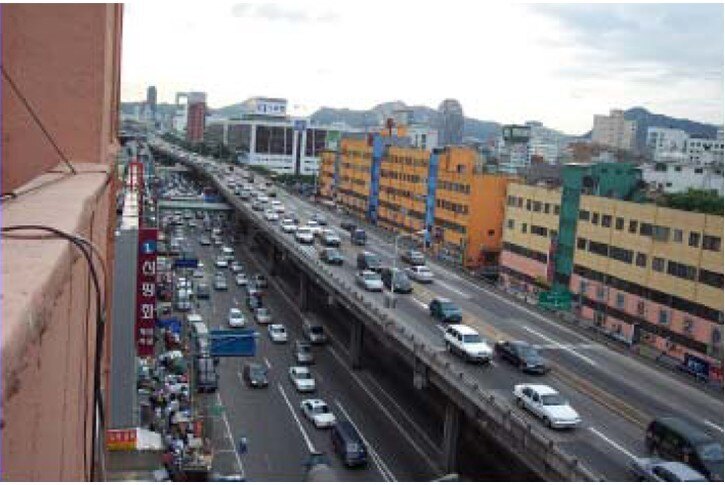 A busy dual carriage motorway in South Korea with high rise building on either side.