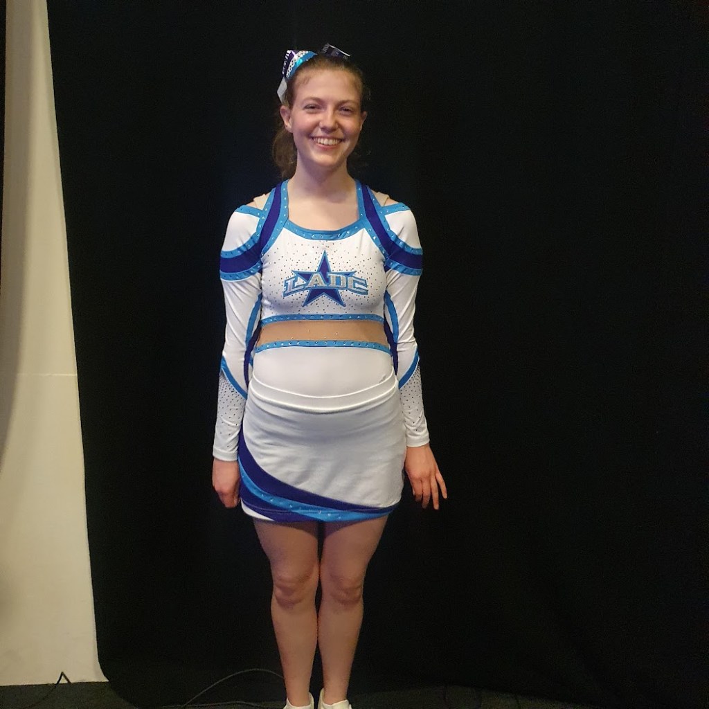 Elizabeth in her cheer outfit smiling. It's white with some blue stripes