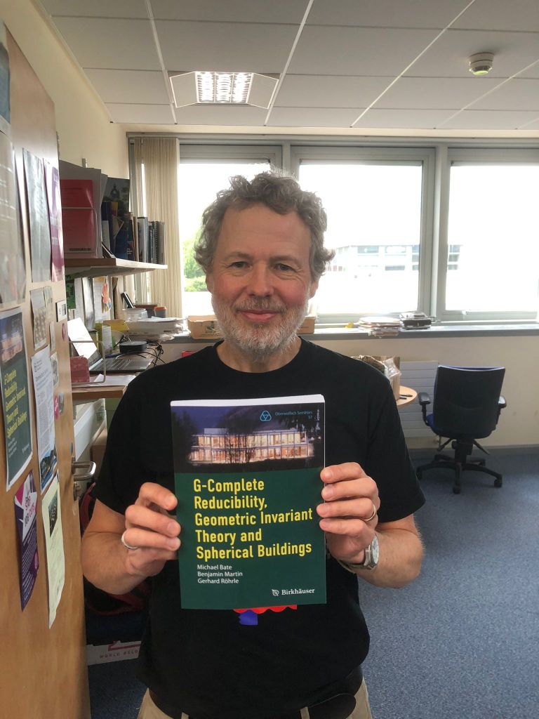 Ben holding his new book. It has a green cover and a photo of Oberwolfach at the top.