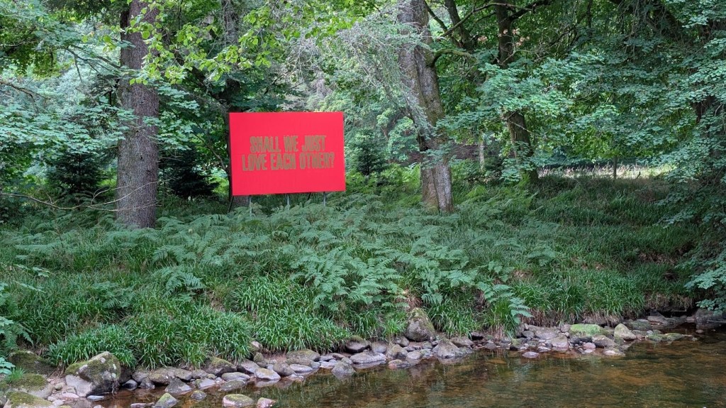 A sign by the river saying "Shall we just love each other"