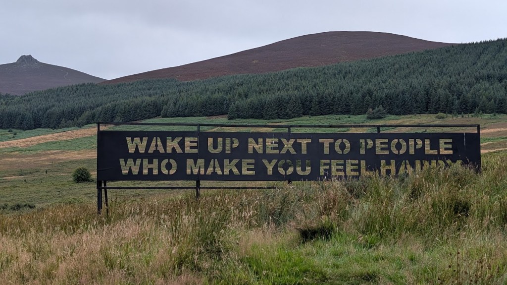 A sign saying Wake up next to people who make you feel happy with Clachnaben in the background.