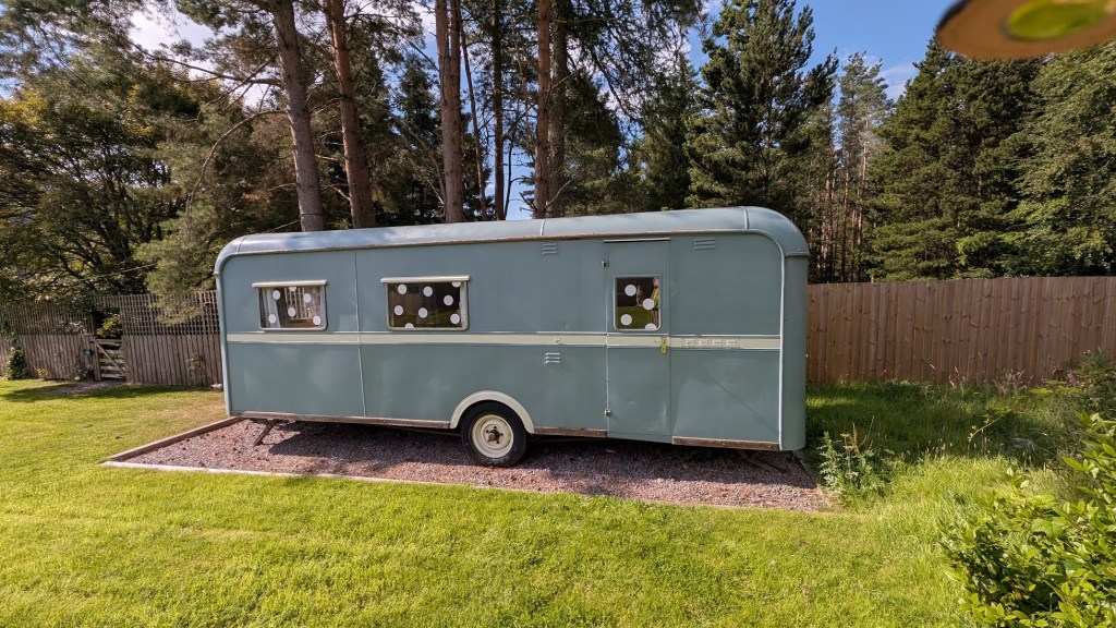The Showman's Caravan from the outside. A vintage blue caravan with three windows and a door.